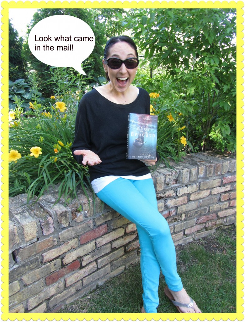 picture of me on a brick retaining wall in blue pants holding the book lies beneath